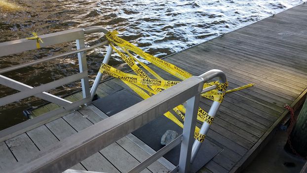 yellow cauton do not enter tape with wood pier and river water