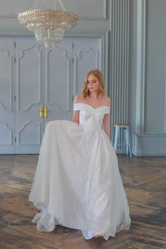 The bride in a beautiful white wedding dress enters the hall holding the hem of the dress