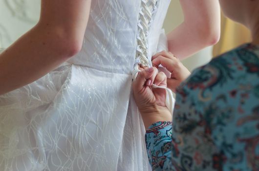 Mother of the bride helps to lace up the dress at the back.Bride puts on a wedding dress in the room