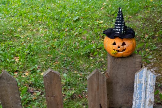 A cheerful pumpkin in a Witch's hat is sitting on the fence.The Concept Of Halloween.