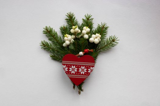 Christmas bouquet with fir branches, red wooden heart and white dogwood berries on a white background . Christmas card. The theme of a winter holiday. Happy New Year.