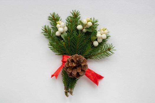 Christmas bouquet with fir branches, red bow, pinecone and white dogwood berries on a white background . Christmas card. The theme of a winter holiday. Happy New Year.