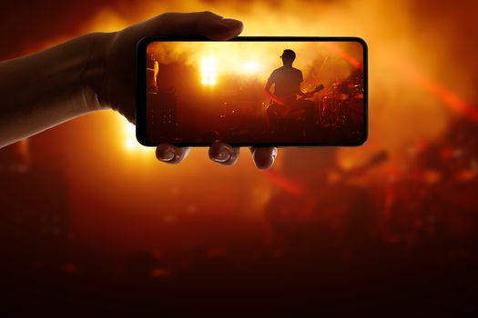 Hand with smartphone records live music concert. Using a mobile phone at the show