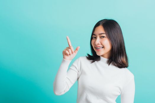 Portrait of Asian teen beautiful young woman smile have dental braces on teeth laughing point finger side away blank copy space, studio shot isolated on blue background, medicine and dentistry concept
