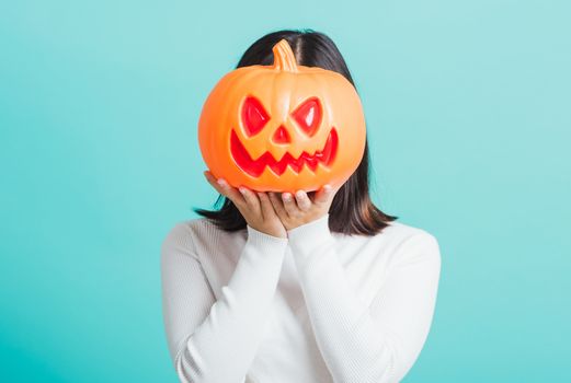 Portrait of Asian beautiful young woman holding orange model pumpkins at her head, funny happy female with ghost pumpkins, studio shot isolated on blue background