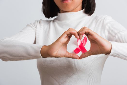Breast cancer awareness healthcare and medicine concept. Close up Asian woman wear shirt she have pink breast cancer awareness ribbon on chest show symbol heart framing from fingers, white background
