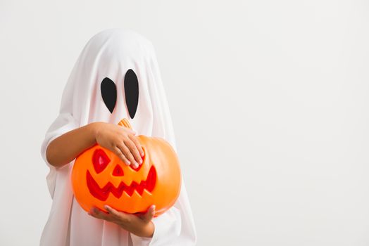 Funny Halloween Kid Concept, little cute child with white dressed costume halloween ghost scary he holding orange pumpkin ghost on hand, studio shot isolated on white background