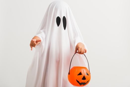 Funny Halloween Kid Concept, little cute child with white dressed costume halloween ghost scary he holding orange pumpkin ghost on hand, studio shot isolated on white background