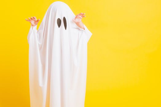 Funny Halloween Kid Concept, Closeup a little cute child with white dressed costume halloween ghost scary, studio shot isolated on yellow background