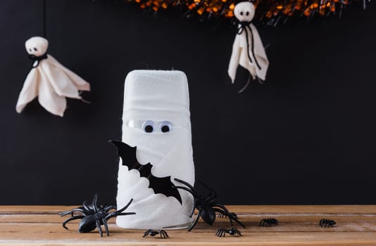 Funny Halloween day decor party concept, The mummy ghost on water glass wrapped around with bandage and have bats and spider stick it found only eyes, studio shot isolated on black background