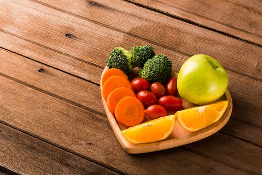 Top view of fresh organic fruits and vegetables in heart plate wood (apple, carrot, tomato, orange, broccoli) on wooden table, Healthy lifestyle diet food concept
