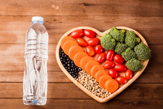 Top view of fresh organic fruits and vegetables in heart plate wood (carrot, Broccoli, tomato) and plastic water bottles on wooden table, Healthy lifestyle diet food concept