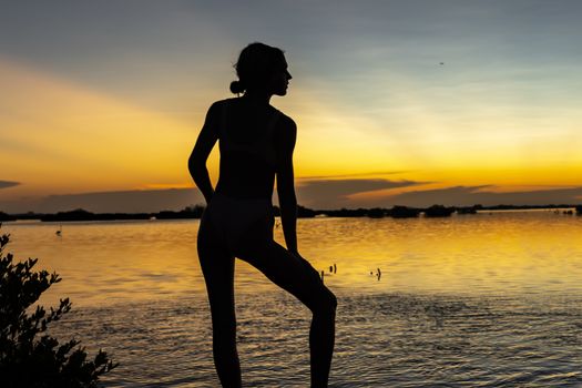 A beautiful latin model is silhouetted as she poses with the rising sun behind her on a exotic Caribbean beach