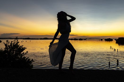 A beautiful latin model is silhouetted as she poses with the rising sun behind her on a exotic Caribbean beach