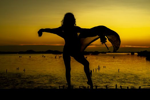 A beautiful latin model is silhouetted as she poses with the rising sun behind her on a exotic Caribbean beach