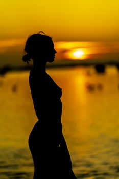 A beautiful nude latin model is silhouetted as she poses with the rising sun behind her on a exotic Caribbean beach