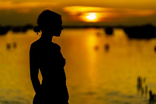 A beautiful nude latin model is silhouetted as she poses with the rising sun behind her on a exotic Caribbean beach
