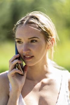 A gorgeous blonde model talks on her cellphone on an autumn day outdoors in a park