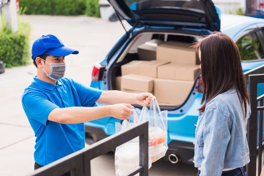 Asian young delivery man wear face mask he making grocery service giving rice food boxes plastic bags to woman customer receiving door at house after pandemic coronavirus, Back to new normal concept