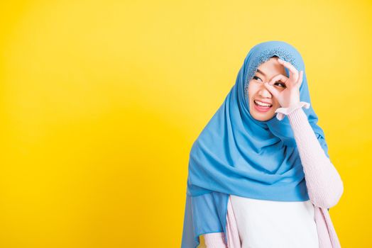 Asian Muslim Arab, Portrait of happy beautiful young woman Islam religious wear veil hijab funny smile she show gesture fingers in okay gesture symbol, OK sign over her eyes isolated yellow background