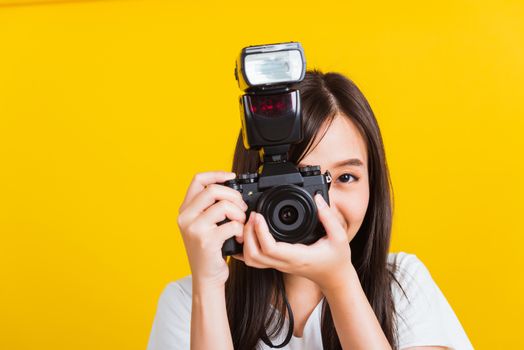 Portrait of happy Asian beautiful young woman photographer smile take picture and looking viewfinder on retro digital mirrorless photo camera ready to shoot, studio shot isolated on yellow background