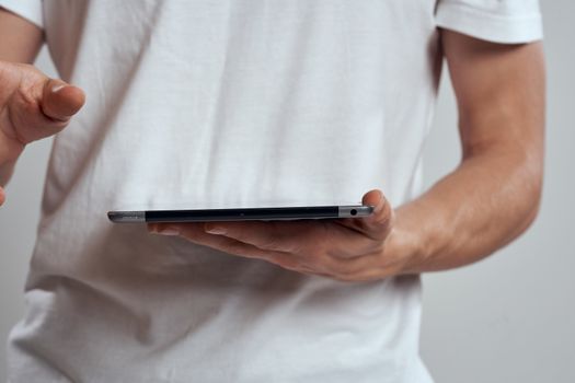 Tablet with a touch screen on a light background male hands white t-shirt cropped view. High quality photo