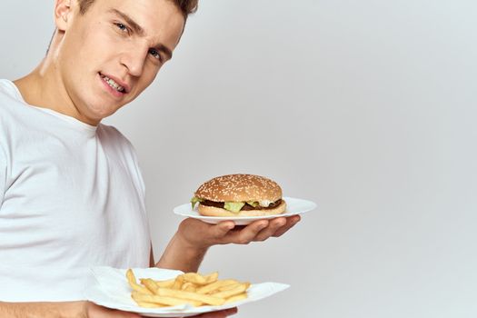 a man with fries and a hamburger on a light background in white t-shirt close-up cropped view Copy Space Model. High quality photo