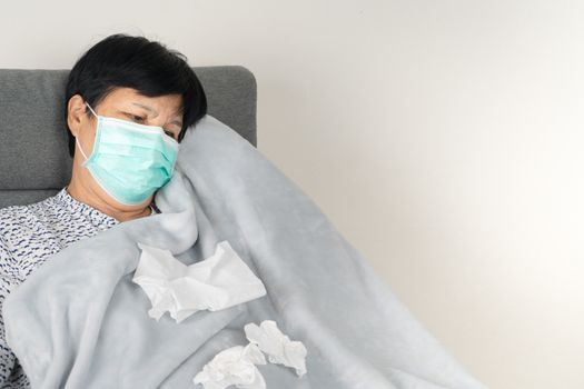 sick senior woman wearing mask with dirty tissue. ill person wearing blanket woolen lay down on sofa