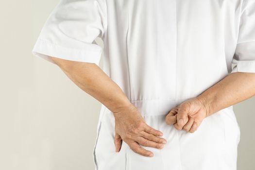 senior doctor woman suffering of backache, touching back with hand, muscular pain over white background