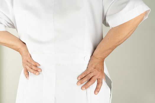 senior doctor woman suffering of backache, touching back with hand, muscular pain over white background