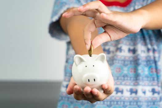 Money saving and donation concept, child put money on cute white piggy bank