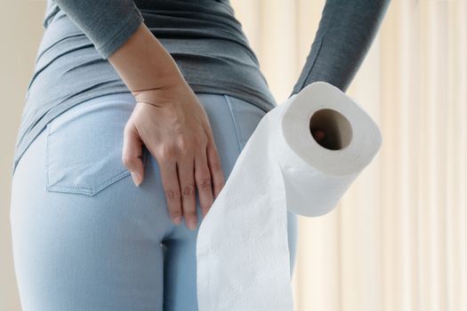 Disorder, Diarrhea, incontinence. Healthcare concept. Woman hand holding her bottom and tissue or toilet paper roll.