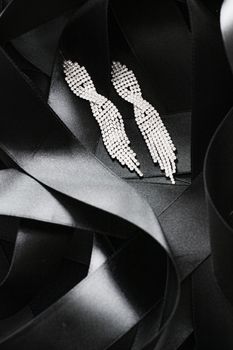 Luxury diamond earrings on black silk ribbon as background, jewelry and fashion brands