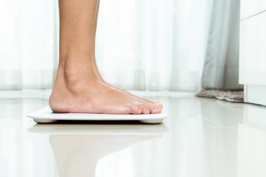 Overweight female is standing on white scales at home