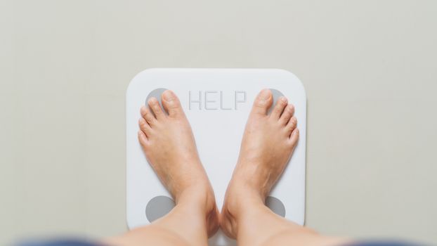 Overweight female is standing on white scales at home with HELP word