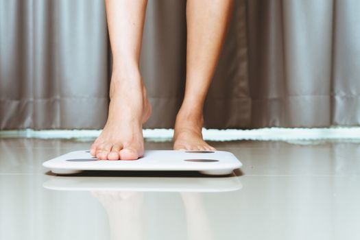 Female leg is stepping on white scales at home