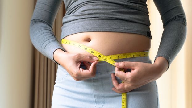 Fat woman hand holding measurement tape on her belly fat. woman diet lifestyle and build muscle concept.