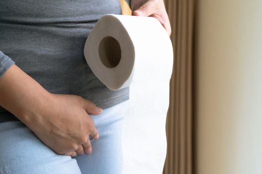 Disorder, Diarrhea, incontinence. Healthcare concept. Woman hand holding her crotch lower abdomen and tissue or toilet paper roll.