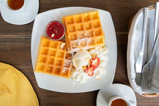 waffle topped with strawberry syrup, icecream, whipped cream and almond slice