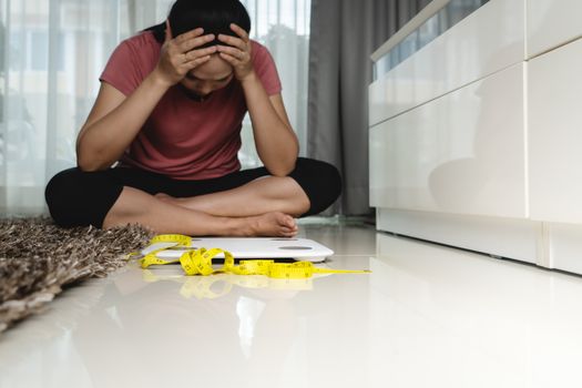 Weight loss fail concept. Scale and measure tape with depressed, frustrated and sad woman sitting on floor - soft focus on measure tape