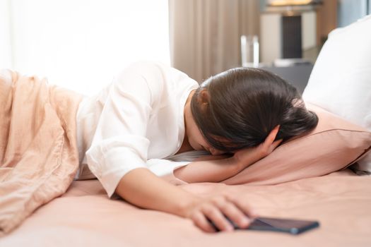 sleepy woman turn off alarm on smartphone while sleeping in bed