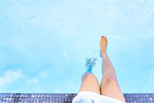 Girl legs in the blue swimming pool,   Summer holiday concept.