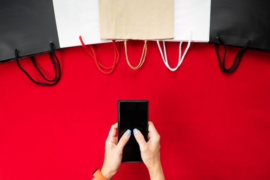 black friday sale, woman hand online shopping on smartphone with shopping bag on red background