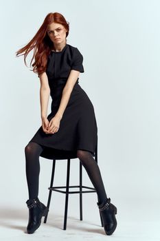 woman high chair indoors full length black dress red hair model boots. High quality photo