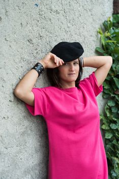 girl with dark hair posing wearing a black beret and a fuchsia dress and a bracelet, image of a woman posing in front of a light wall