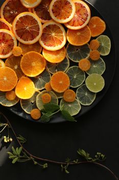 fresh slices of citrus fruits on black round plate on black background. Sours of vitamin C, healthy life concept, vibrant color concept. Top view, flat lay