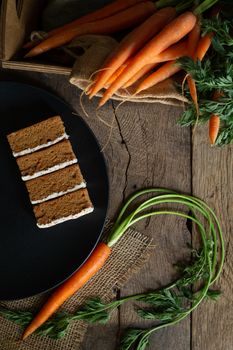 Fresh organic carrots, carrots cakes on black plate, canvas on antique wooden table. Rustic kitchen concept. Banner, poster, mock up. Grunge, vintage, rustic style