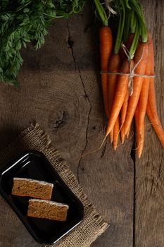 Fresh organic carrots, English carrots cakes on black plate, canvas on antique wooden table. Rustic kitchen concept. Banner, poster, mock up. Grunge, vintage, rustic style