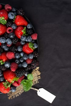 Strawberries, blackberries, raspberries, green mint on canvas and black background with gift tag. Mock up, menu, cafe poster concept