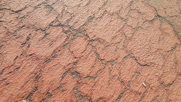 Red colored damaged road or paved pathway with crackes of different shpaes. Cracked texture with copy space for text and messages